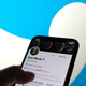 A phone showing Elon Musk's Twitter profile is seen against Twitter's blue bird logo.